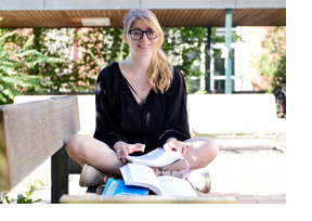 Studentin sitzt auf einer Bank und blättert in einem Buch. (Foto: Julien Fertl)