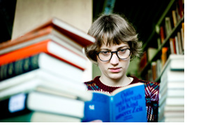 Eine Studentin sitzt vor einem Berg Bücher. (Foto: Johannes Simon)