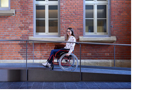 Eine Studentin fährt mit einem Rollstuhl eine Rampe hoch. (Foto: Martin Rehm)